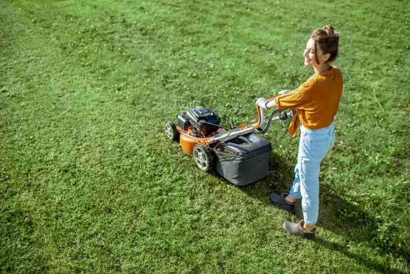 Beautiful young woman cutting grass with gasoline lawn mower, view from above