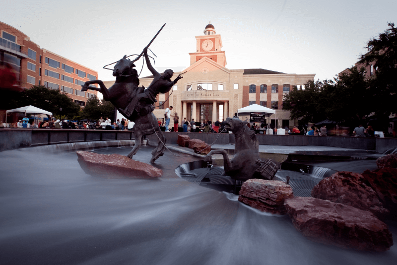 Crowds of people stand between the Stephen F. Austin monument and city hall in Sugar Land, Texas