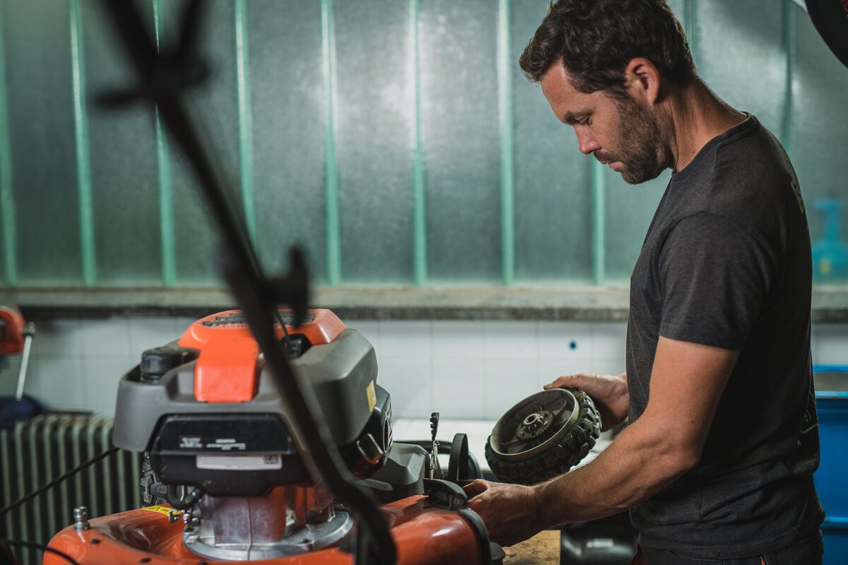 Professional serviceman is repairing a lawnmower, refitting a front wheel. Man repairing a mower in a workshop