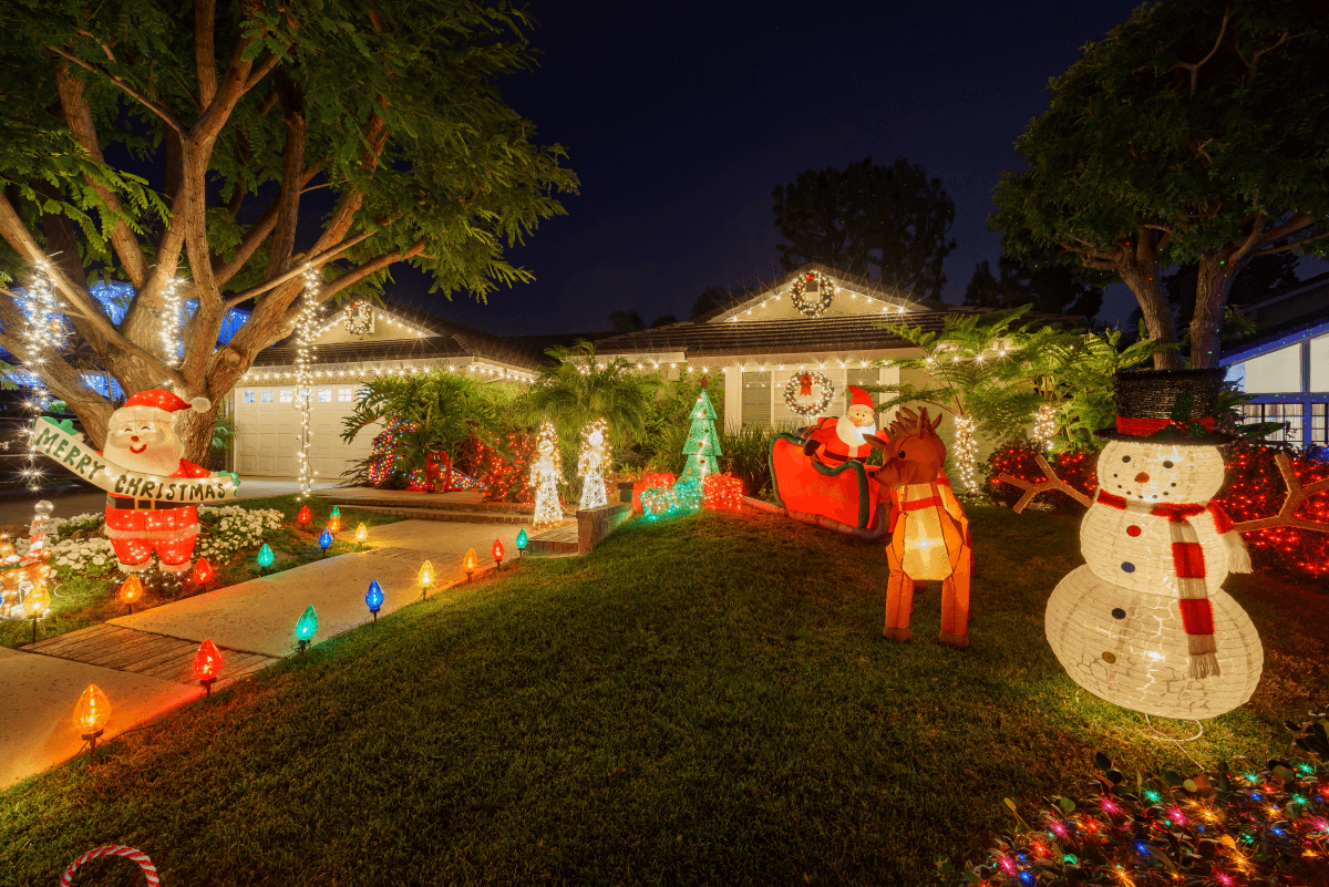 A home exterior and grassy lawn is illuminated by Christmas decorations and holiday figurines