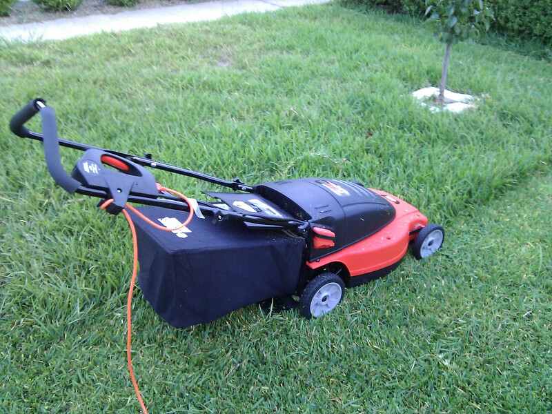 electric, corded lawn mower on a partially mowed lawn