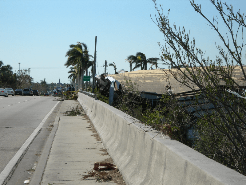 Bent shrubs, a destroyed building on the right, and other debris line a highway in Boca Raton, Florida, after a hurricane.