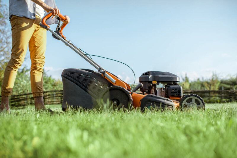 Man cutting grass with gasoline lawn mower on the backyard, cropped image with no face