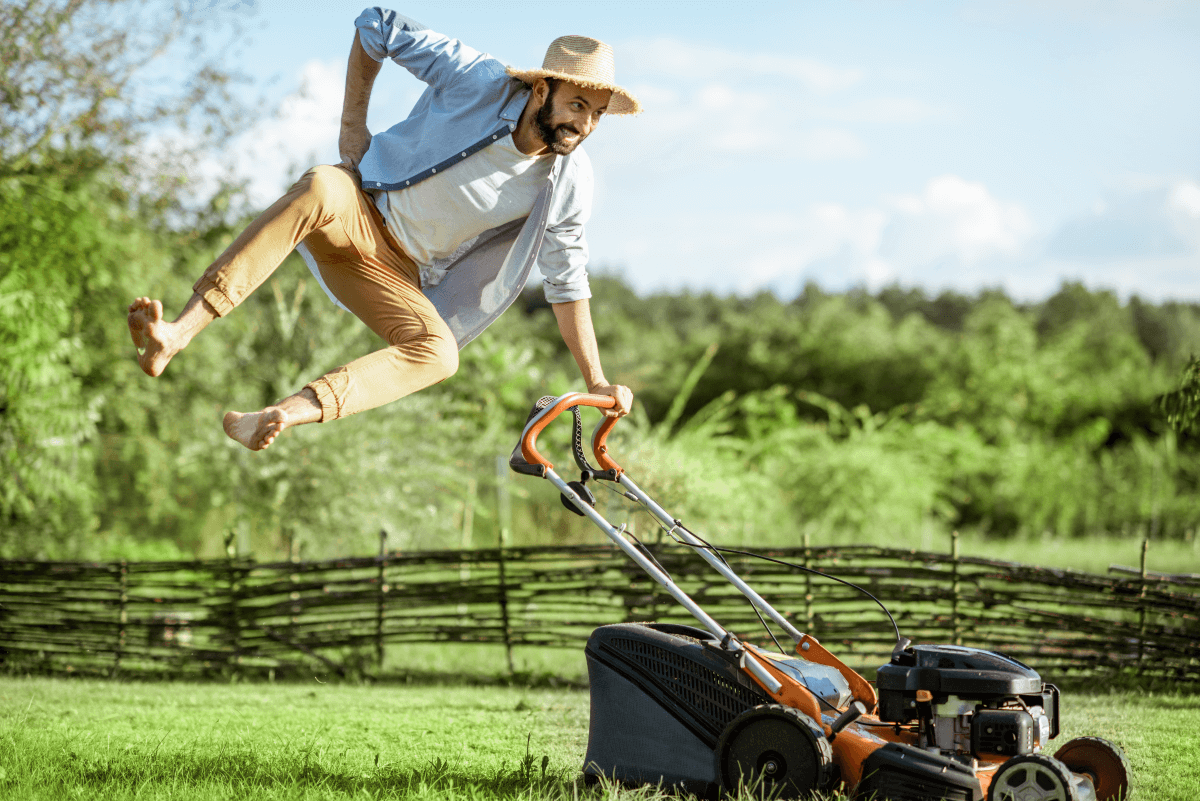 A man jumps barefoot in the air while mowing his lawn