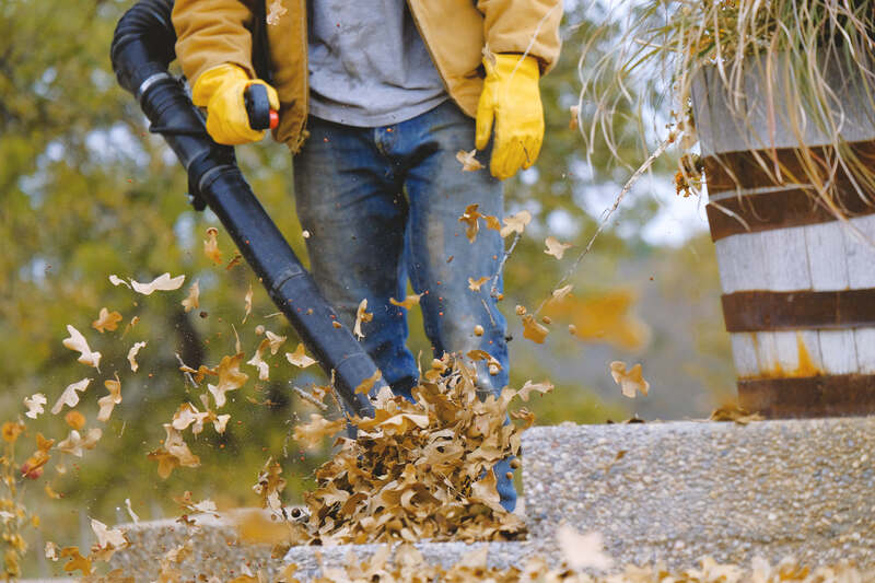 Worker leaf blowing fall leaves off walkway with equipment. Autumn season working lifestyle. 