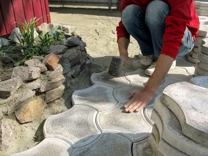 A worker holds a rubber hammer in his hand and does the work of laying paving slabs.