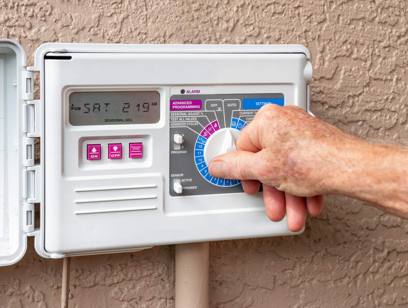 Someone adjusting an automatic sprinkler system timer on a wall