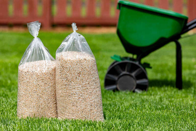 Grass and herbicide fertilizer bags sitting on a grass with a fertilizer extensor in the backyard