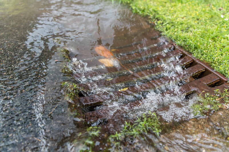 Storm water runoff going down a storm drain next to a lawn