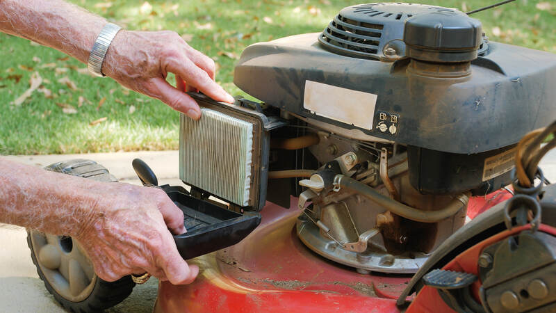 Male landscaper replacing air filter on gas powered lawn mower. Checking air cleaner filter for proper maintenance.